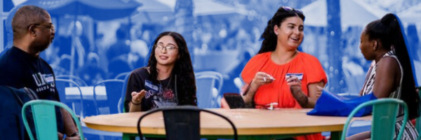 Four alumni (three females and one male) pictured talking at a picnic table.