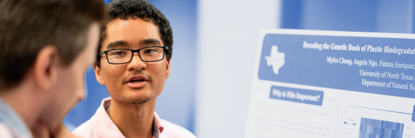 Two men talking with a poster presentation in the background.