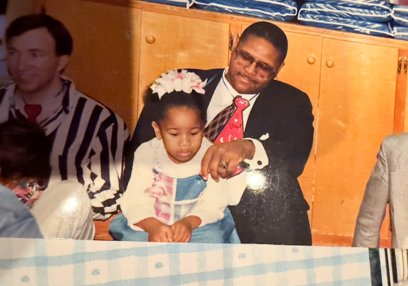 A Young Cora Black Sits on Daddy's Lap at a Family Gathering