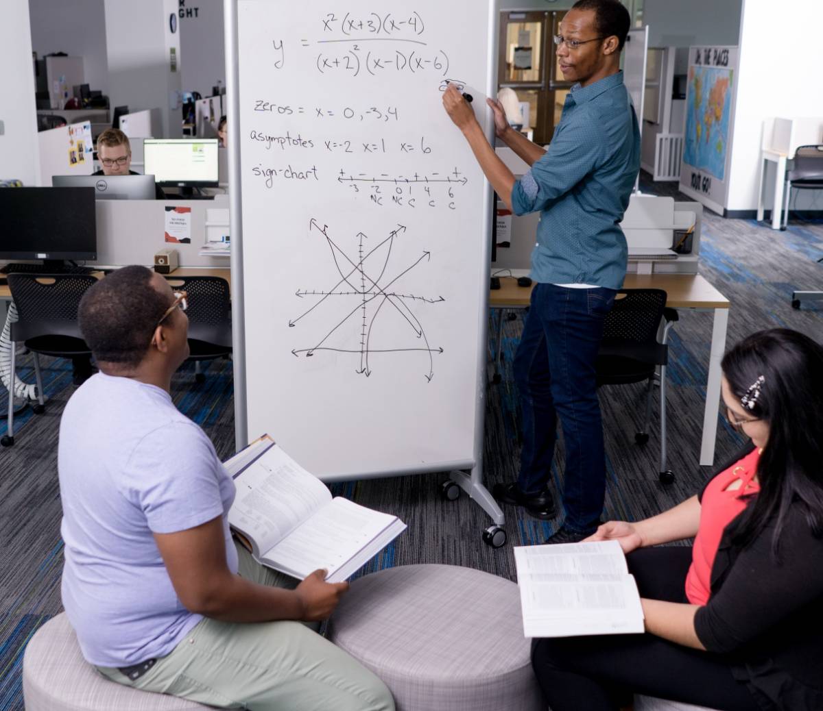 Tutor standing in front of a white board with a math equation written on it looking at a student