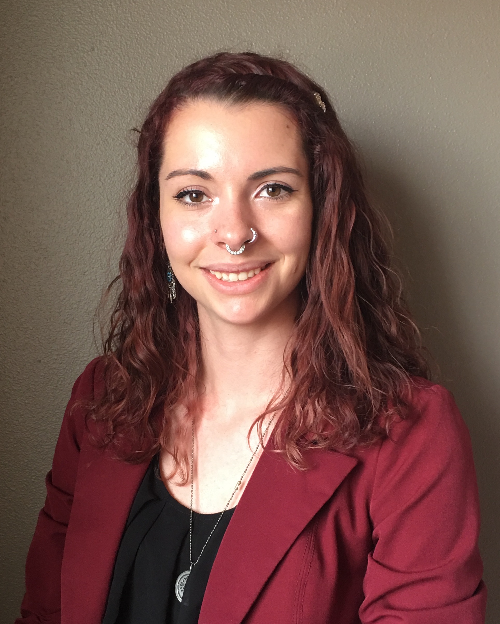 young woman smiling in red blazer with wavy auburn hair