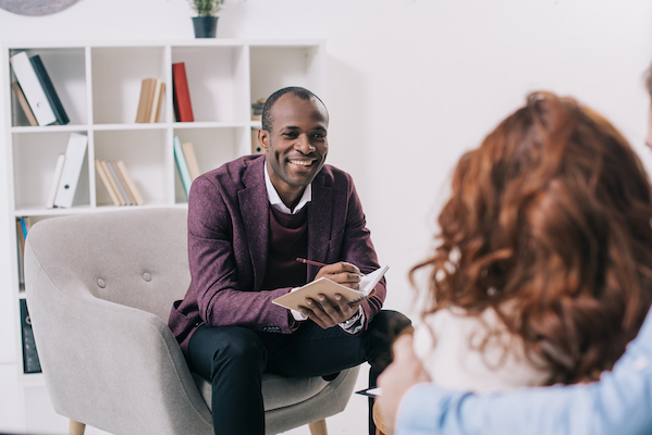 man seated with clipboard speaking to woman