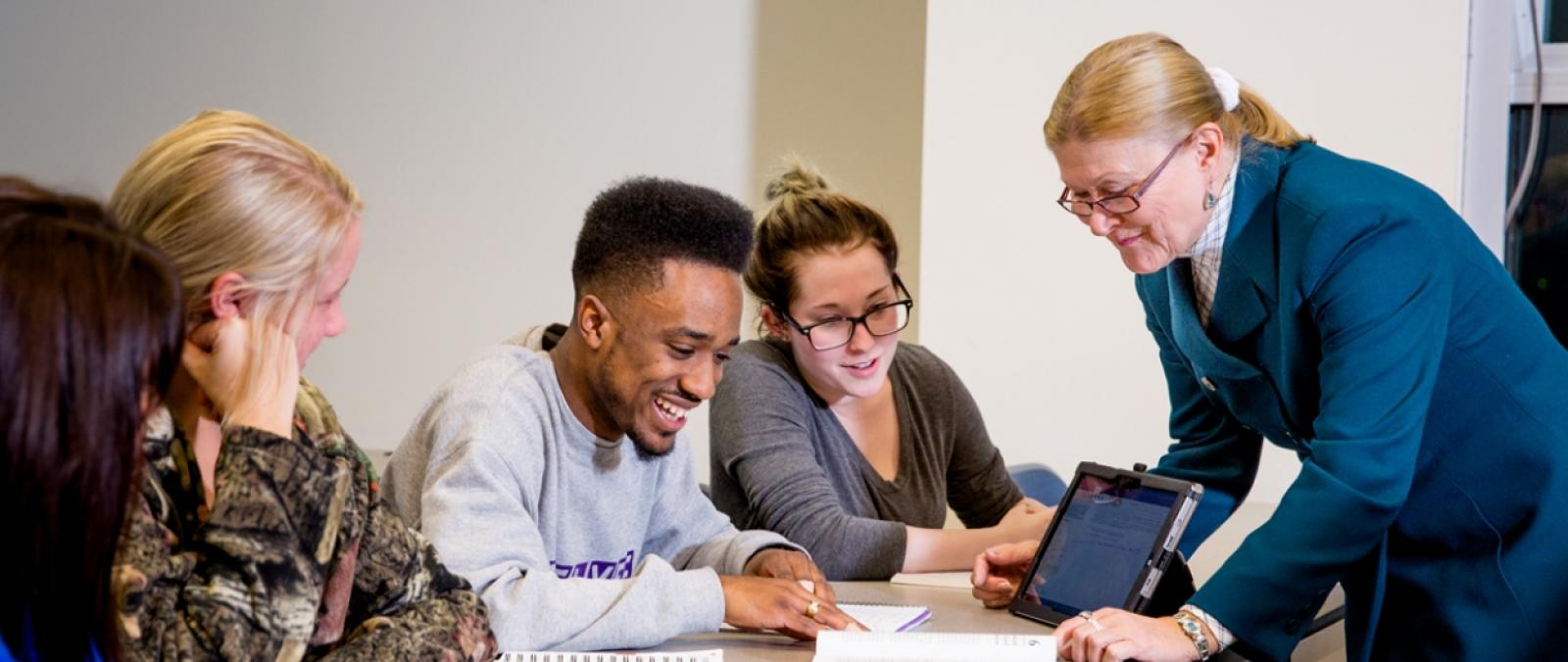 students with professor at table viewing ipad